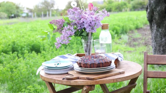 在刮风的春日里，私人花园里盛开的树下，餐桌上有甜蜜的蛋糕和一束鲜花