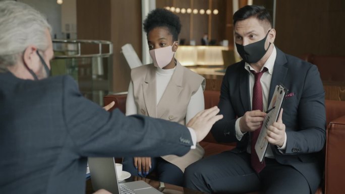 多民族商人戴着医用口罩在酒店大堂洽谈合作