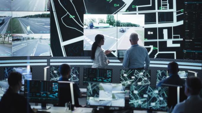 未来城市物流规划监控中心，不同的男性和女性官员在大数字屏幕上分析现场监控录像。优秀的专家团队在办公室