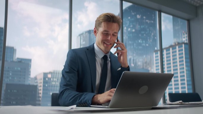 西装革履的自信商人坐在办公室的办公桌前，使用笔记本电脑，用智能手机接听同事的电话。成功的销售经理讨论