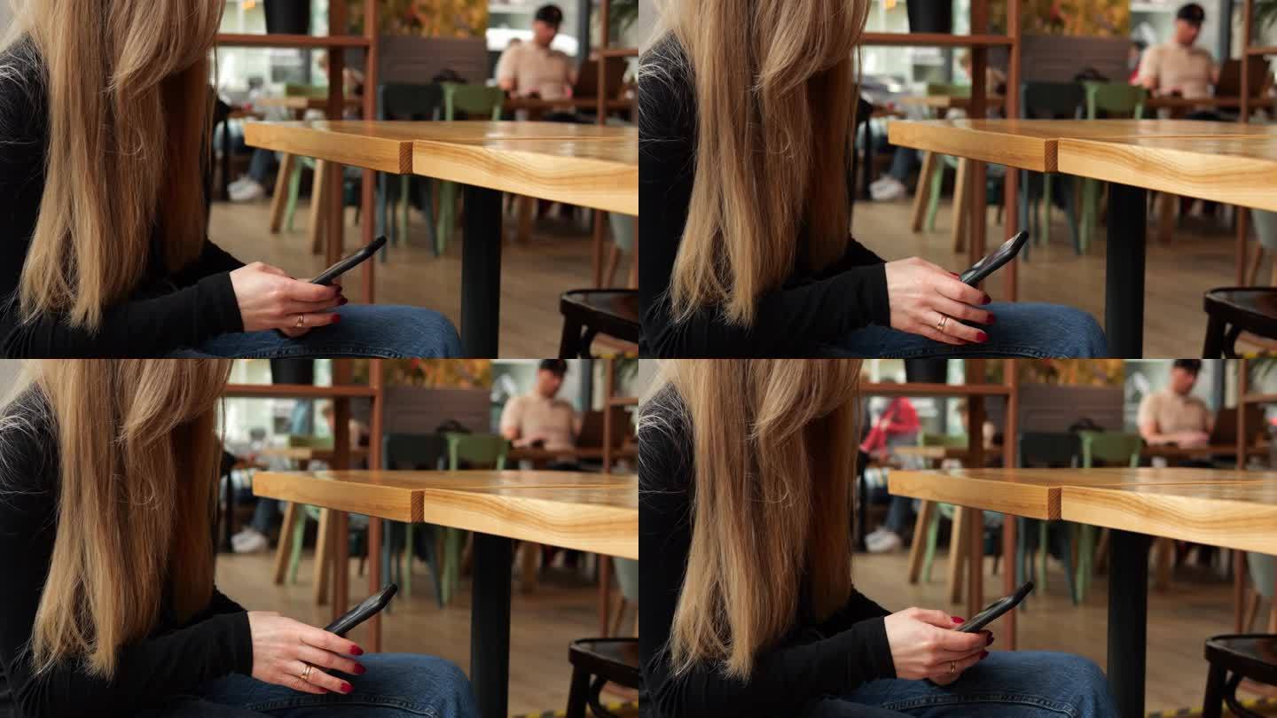 一个陌生的年轻女子在咖啡店里等着点餐，手机放在膝盖上。留着棕色长发的无名女子坐在智能手机上的空桌子旁
