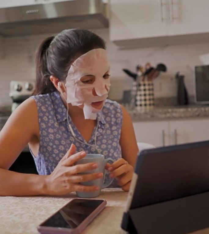 视频通话中的西班牙裔年轻女子一边看着厨房里的镜子，一边给自己敷上保湿、营养、透明质酸和祛痘面膜的慢动
