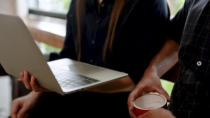 特写手亚洲女人坐着，拿着笔记本电脑，用右手式指着屏幕，丈夫看着工作正在做，请教听丈夫的意见，是业通。