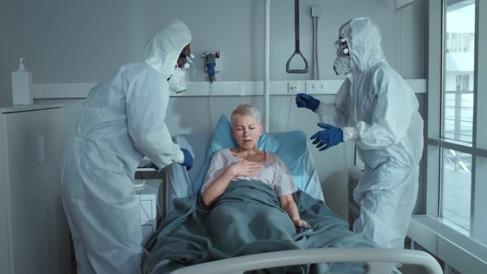穿着个人防护服的医护人员正在检查躺在病床上戴着氧气面罩呼吸机的女病人