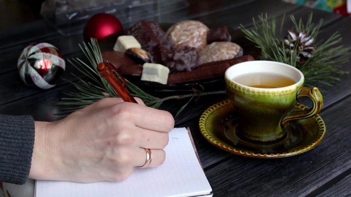 写下新年计划的要点。一个女人的手特写。圣诞装饰。茶和糖果。Hygge