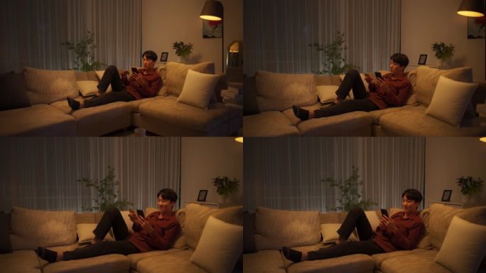一个时尚的韩国男人躺在舒适客厅的沙发上，用智能手机网购。亚洲男性在移动电子商务应用中输入信用卡信息