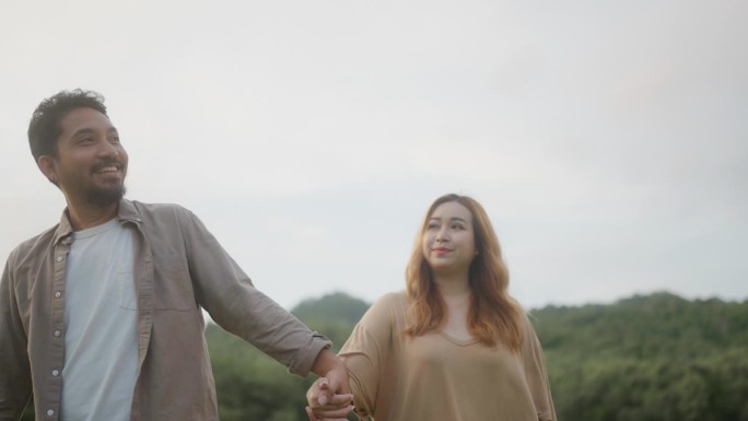度假的亚洲夫妇微笑着手牵着手走在草地上。