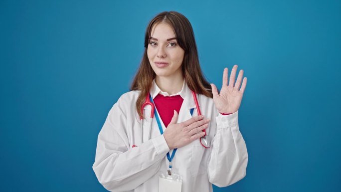 年轻的西班牙女医生在孤立的蓝色背景下手放在胸前宣誓