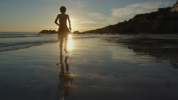 男孩在海滩上奔跑，在夕阳下的水波中戏水