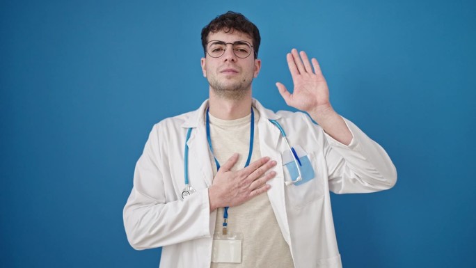 年轻的西班牙裔医生在孤立的蓝色背景下把手放在胸前宣誓