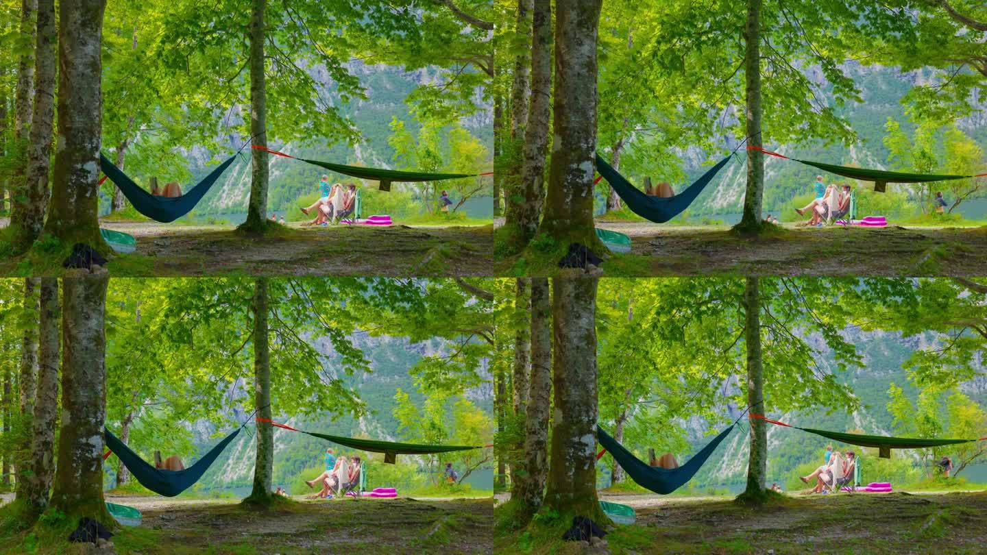 度假时人们在森林里露营。一个女人在湖边的吊床上休息