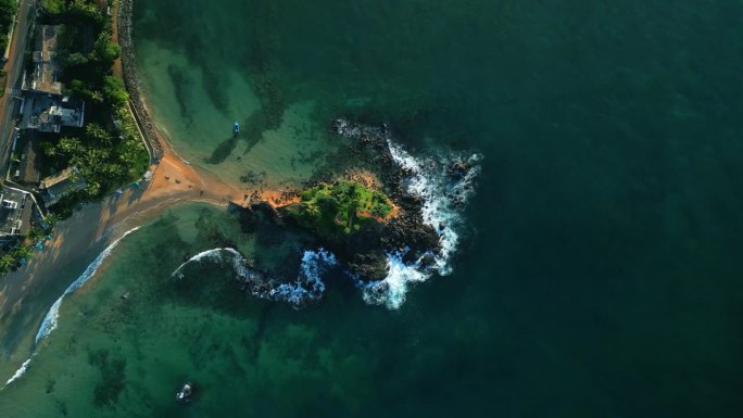 绿色的热带岩石岛，在蓝绿色的海洋中间，被海浪冲刷着。无人机拍摄的画面显示，斯里兰卡米瑞萨的鹦鹉岩被波