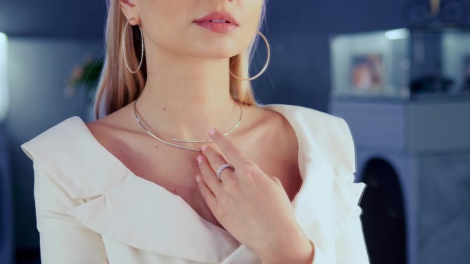 美得惊人的模特站在珠宝店的镜子前试戴一条闪闪发光的金钻石项链。在一家豪华的精品店里，女孩戴着金色的珠