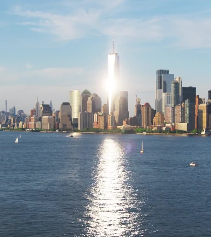 垂直屏幕:航拍镜头的相机接近曼哈顿岛与办公室和公寓大楼。哈德逊河风景与游艇，船只和太阳反射从摩天大楼