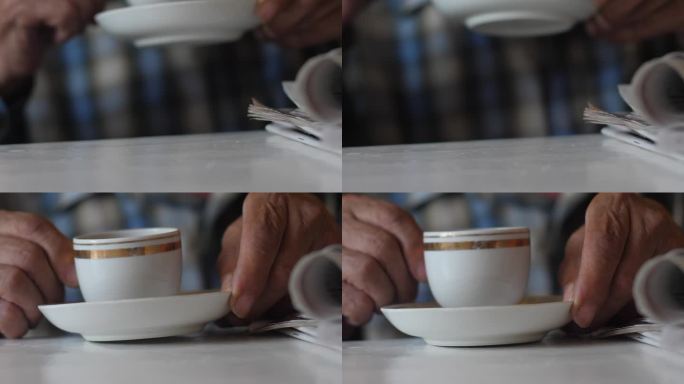 退休老人看完晨报，用杯子喝着浓香的茶。老人的居家休闲。一个老人端着一杯咖啡的手