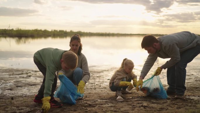 幸福的家庭和孩子们在湖边收集塑料垃圾，击掌庆祝胜利