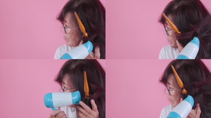 老妇人用吹风机在粉红色的背景上吹干她的头发