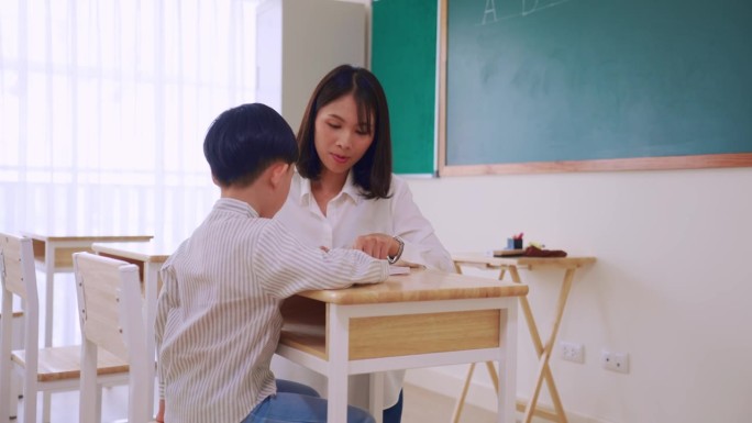 亚洲美女女老师在教室里教小男生。在幼儿园，有魅力的女教师在课堂上给孩子们讲解和教育课程。