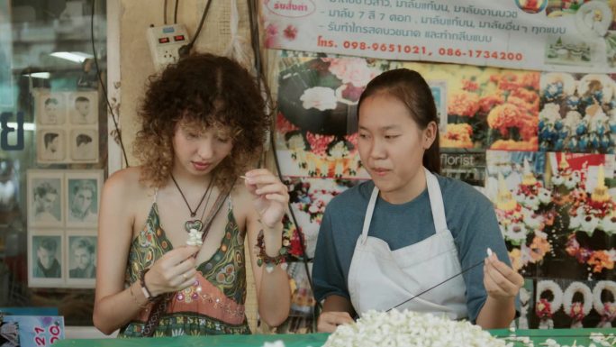 在pak khlong talat，亚洲女店主flower教一名女游客自己制作花环。