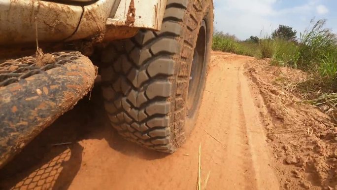 在土路上奔跑的视角。越野车的车轮行驶在尘土飞扬的肮脏道路上，湿的和干的泥。在穷乡僻壤旅行的观点