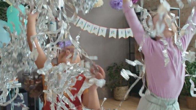 两个快乐的多元化女孩在生日派对上玩着成堆的金箔