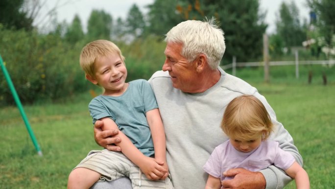 爷爷和孙子在公园散步时玩得很开心。快乐的家庭时光。老人爷爷抱着男孩和女孩。夏天的一天。微笑的老男人和