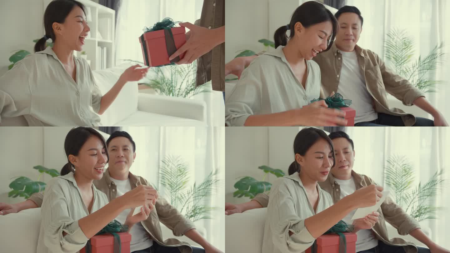快乐的亚洲夫妇坐在家里客厅的沙发上，用红色礼盒送生日礼物，玩得很开心。生活方式花时间在家里。
