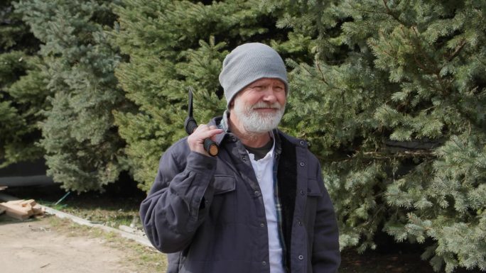 一个英俊的老人，戴着帽子，留着灰白的胡子，拿着斧头准备砍树，背景是云杉，特写