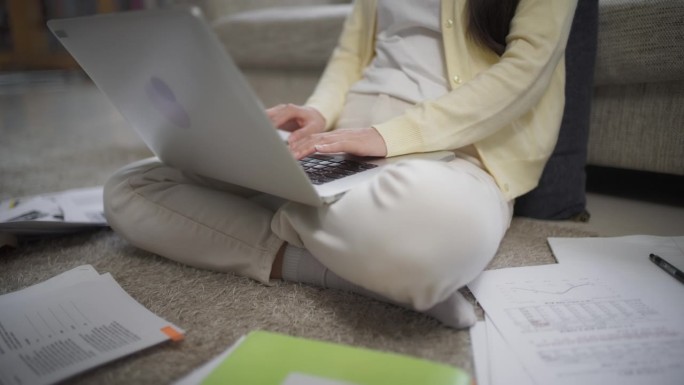 近距离观察女学生写论文、上网研究、在家使用笔记本电脑和笔记本。年轻女子坐在客厅地板上敲键盘