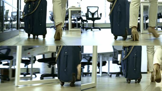 一个女人的腿的特写，她带着行李箱走过办公室的走廊