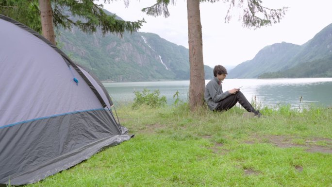 视频4k PRORES HQ。在夏日的绿色森林里，一个年轻的白人孩子躺在露营帐篷附近的草地上，用他的