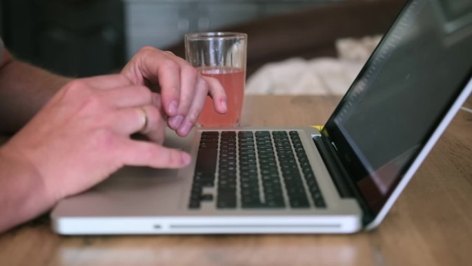 戴着婚戒的男性双手正在木桌上的笔记本电脑上打字