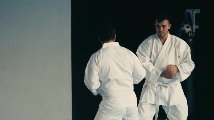 两名身穿白色和服的男子在健身房练习与头部高度相等的踢腿，练习跆拳道