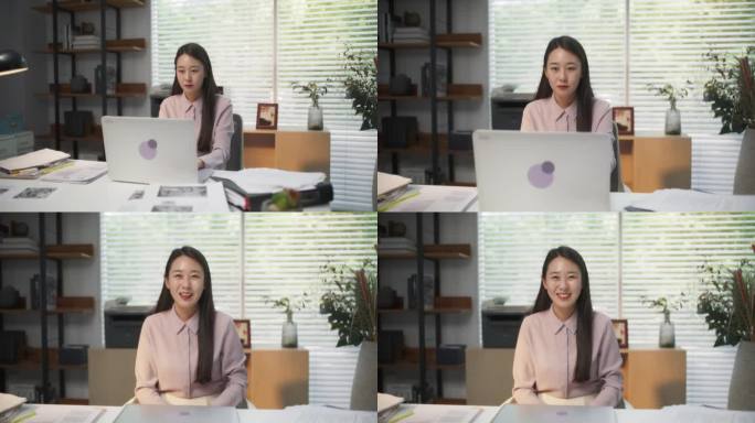 一个美丽的韩国女性在一个时尚的创意机构的桌子后面的电脑前工作的肖像。年轻快乐的女人合上她的笔记本电脑
