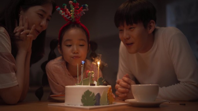 家庭回忆:可爱小女孩在吹灭生日蛋糕蜡烛前许愿的慢动作肖像。年轻的韩国夫妇庆祝他们的女儿长大，鼓掌欢呼