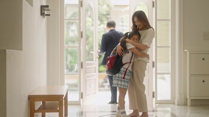 小女孩早上抱着妈妈离开家去上学，说再见。亚洲家庭准备在女儿上学的第一天去学校。