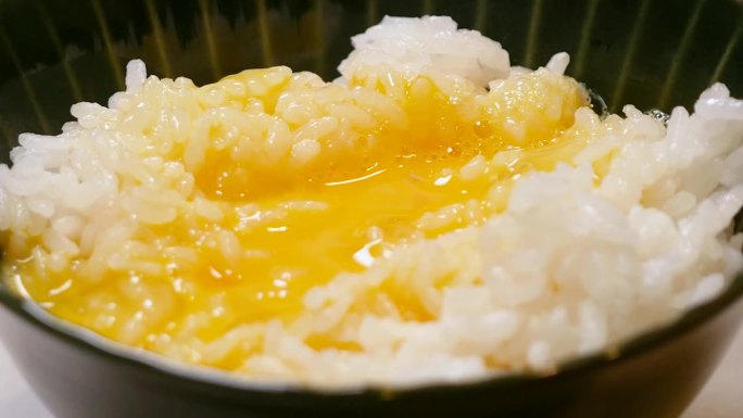 白米饭加生鸡蛋。一个将生鸡蛋和酱油倒入新鲜煮熟的米饭的视频