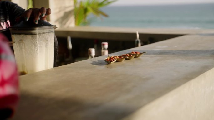 一些可爱的小盘子里的小吃在海景户外吧台。吧台后面的调酒师用搅拌机调制奶昔和冰沙，欣赏海景。夏季露天吧