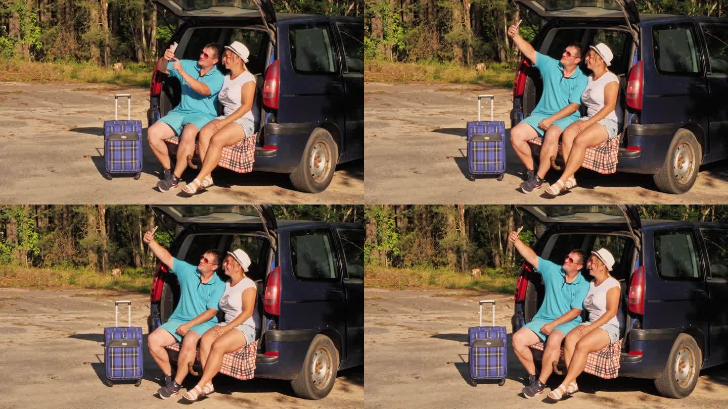 一对可爱的旅行者夫妇坐在汽车后备箱里用手机自拍。旅行者会在路边的森林里停下来自拍，作为他们冒险的纪念