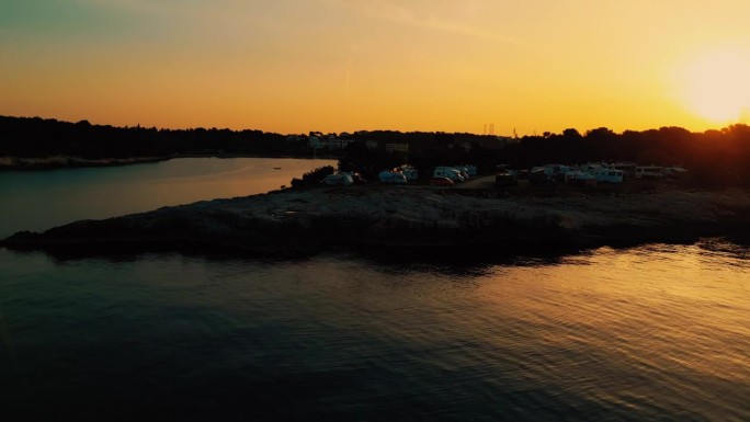 无人机露营地，在日落时橙色的天空下，房车停在海边