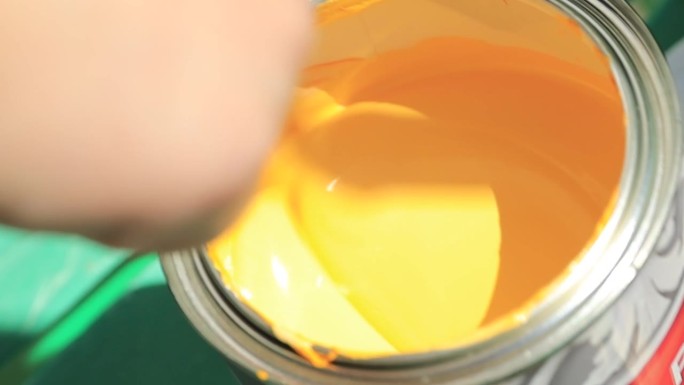 手搅动着罐子里的黄色颜料