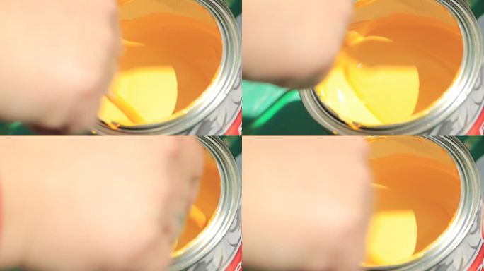 手搅动着罐子里的黄色颜料