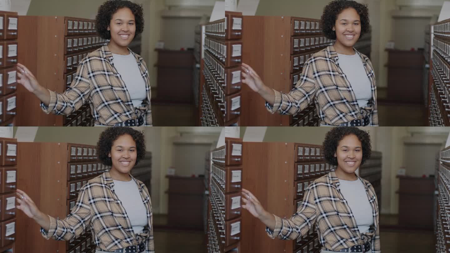 聪明的非裔美国女学生站在图书馆里微笑着看着镜头