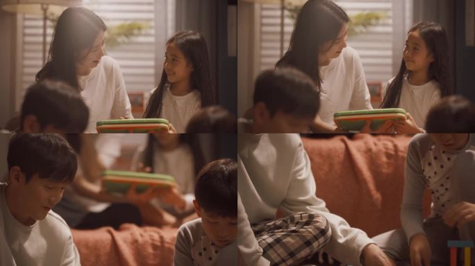 一个年轻的韩国家庭在儿童室一起玩耍的肖像。母女玩平板电脑，父子用积木搭房子