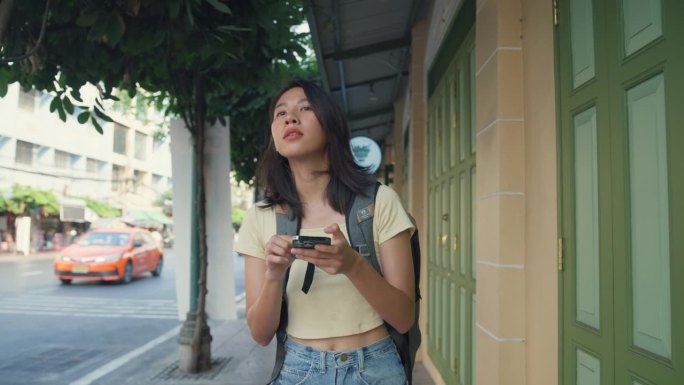 年轻的亚洲女性背包客在城市街道上使用手机。假日度假旅行。