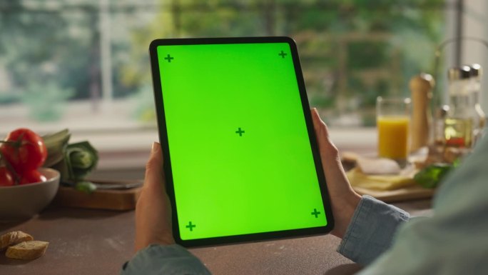 匿名妇女在厨房拿着平板电脑模拟绿屏Chromakey显示器双手。女厨师通过数字内容分享她的食谱，营销
