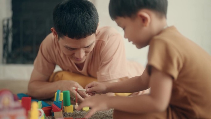 温馨的快乐时刻:亚洲父亲和儿子在舒适的客厅里玩耍。