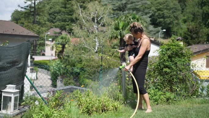 母亲抱着女婴在户外给花园浇水