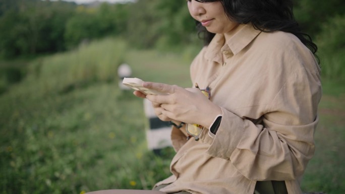 年轻的亚洲女子用手机发短信和滚动在河边的自然。她在欣赏美丽的景色。美丽的女孩深呼吸，