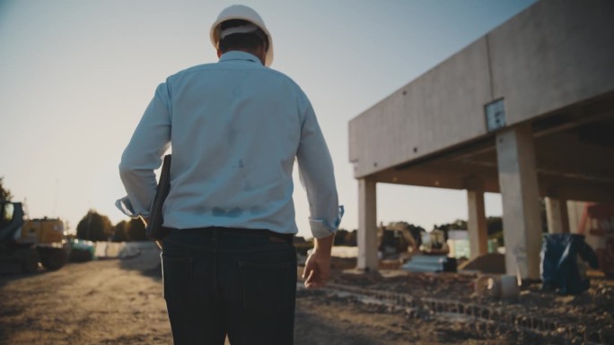 男工头带着笔记本电脑在建筑工地走着